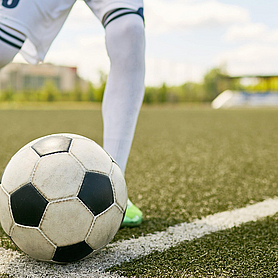 Ein Fußballspieler ist kurz davor einen Eckball zu schießen. Zu sehen sind nur Ball und Beine des Spielers.